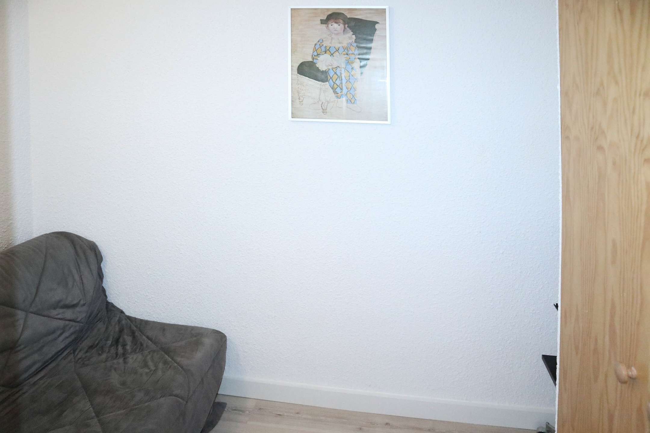 Una stanza con un divano grigio, un quadro appeso al muro e una porta in legno.