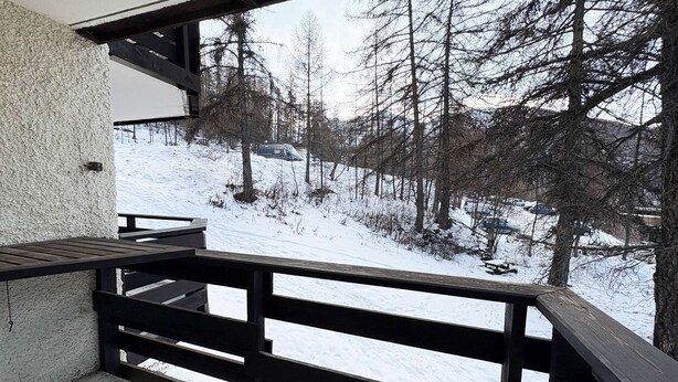Ein Balkon mit Blick auf eine verschneite Landschaft und kahle Bäume.