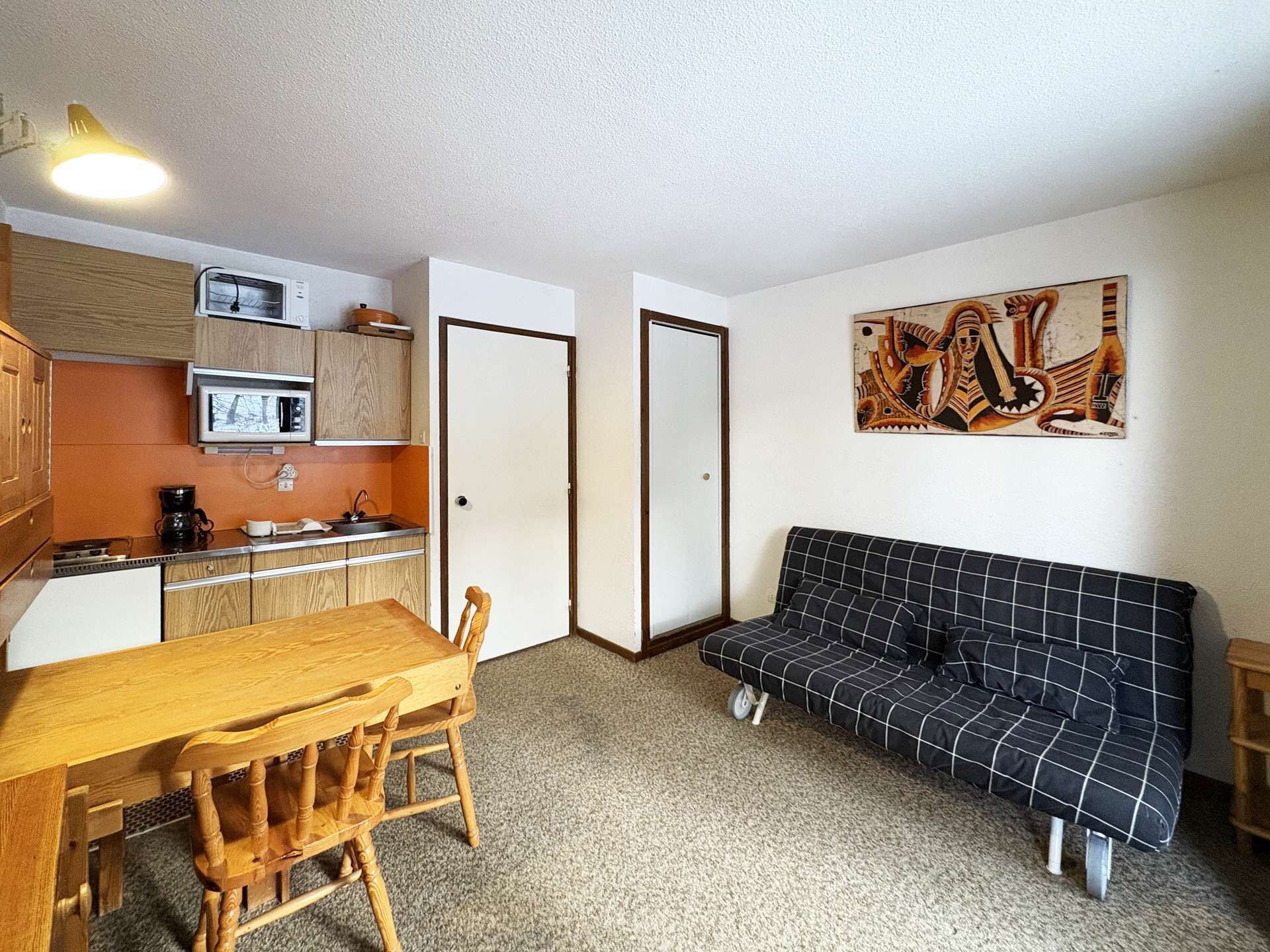 A compact living space with a kitchenette, a dining table with chairs, a sofa, and a single door.