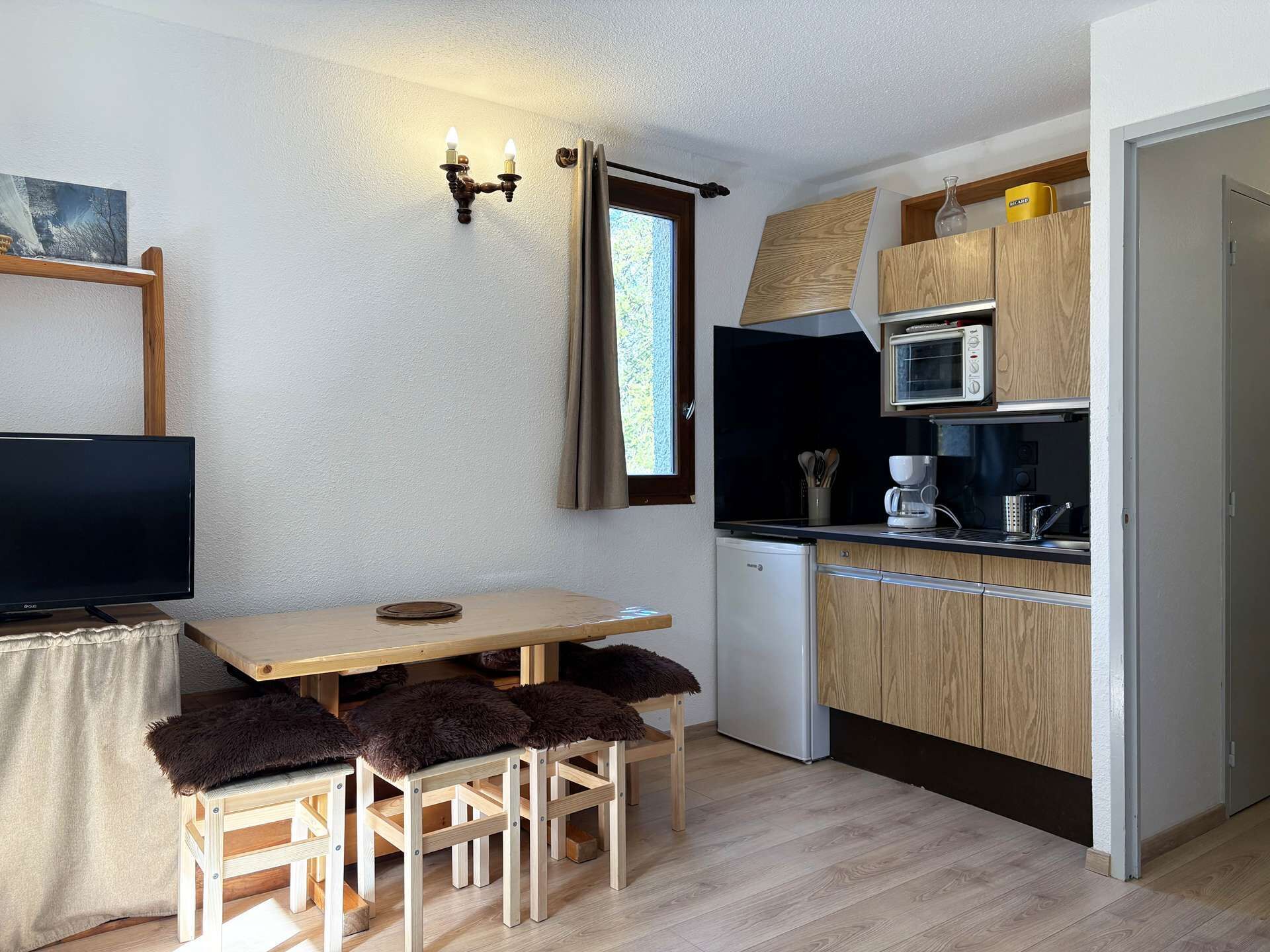 Une cuisine de taille réduite avec une table en bois, un téléviseur et un réfrigérateur.