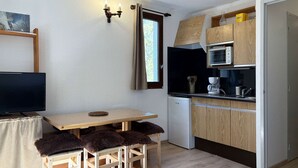 A compact kitchen with a wooden table, a TV, and a refrigerator. - Studio calme pied de pistes (LES ORRES)