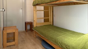 A bunk bed room with a green mattress, a wooden stool, and a small table. - Studio calme pied de pistes (LES ORRES)