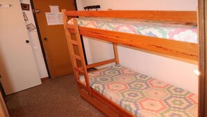 Un llit superposat amb un matalàs estampat, una escala de fusta i una porta amb un tabló d'anuncis.