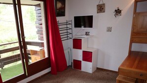 Habitació amb porta de vidre corredissa que dona a un balcó, televisió penjada a la paret, radiador i armari de fusta.