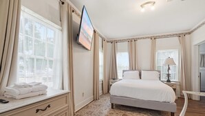 A bedroom with a bed, a TV mounted on the wall, a bedside table with a lamp, and a window with curtains. - Home Away From Home-4 BR Lafayette Stay in the Heart of Town (Lafayette)