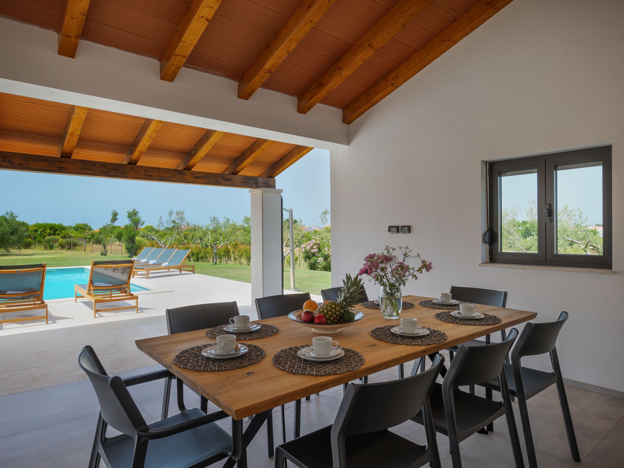A dining area with a wooden table, black chairs, and a view of a swimming pool and greenery.