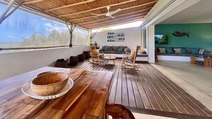 A wooden deck with a ceiling fan, a dining table with a bowl, and a seating area with a sofa and chairs.