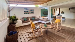 A cozy outdoor seating area with a wooden ceiling, a sofa, two rocking chairs, and a small table.