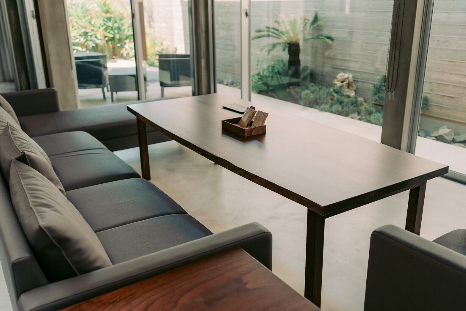 Una sala moderna con un sofá de cuero oscuro, una mesa de centro de madera y un ventanal que da a un jardín.