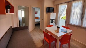 A compact room with a dining table, red chairs, a TV, a microwave, and a small potted plant. - Lovely apartment for 4 guests with WIFI, A/C, TV and balcony (San Michele Al Tagliamento)