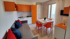 A compact living space with a kitchenette, a dining area, and a sofa with cushions. - Lovely apartment for 4 guests with WIFI, A/C, TV and balcony (San Michele Al Tagliamento)