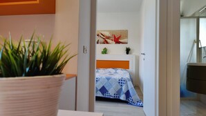 A bedroom with a bed covered in a blue and white checkered blanket, a small plant on the bedside table, and a wall with a starfish and seashell artwork. - Lovely apartment for 4 guests with WIFI, A/C, TV and balcony (San Michele Al Tagliamento)