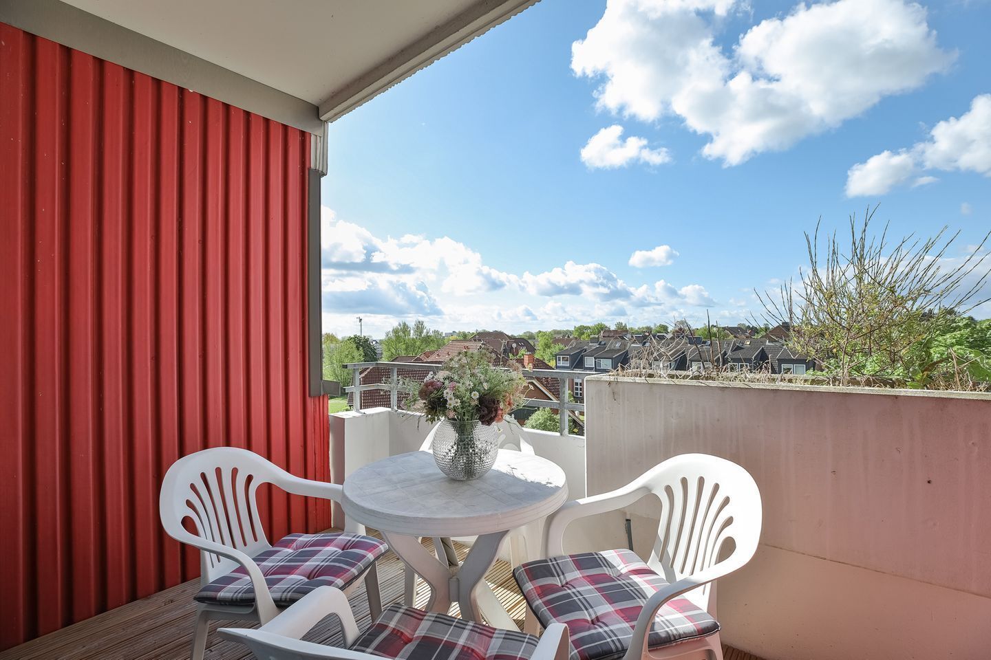 Un balcón con un muro rojo, una mesa blanca con dos sillas y un jarrón de flores.