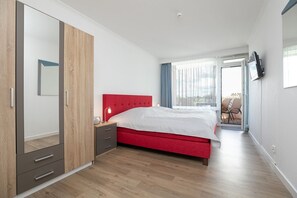 Una camera da letto con un letto rosso, un'armadio in legno e una TV appesa al muro.