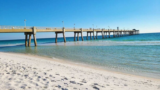 A pier extending into the ocean with clear blue water and a sandy beach.