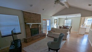 A spacious living room with a fireplace, a sofa, a coffee table, and a dining area in the background.
