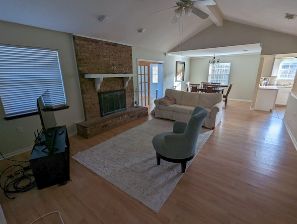 A spacious living room with a fireplace, a sofa, a coffee table, and a dining area in the background. - Gulf Coast Getaway Home-3 bed, 7m walk to bay beach and pier (Mary Esther)