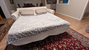 A bedroom with a bed, a red patterned rug, and a kitchen in the background. - Gulf Coast Getaway Home-3 bed, 7m walk to bay beach and pier (Mary Esther)