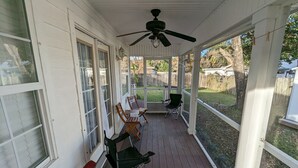 Een overdekte veranda met houten vloer, een plafondventilator en uitzicht op de achtertuin.