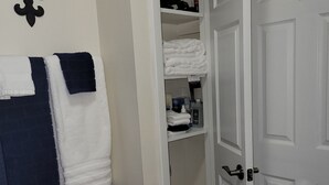 Une salle de bain équipée d’un porte-serviettes où sont rangées des serviettes blanches et bleu marine, d’un support à papier toilette et d’une étagère contenant des articles de toilette.