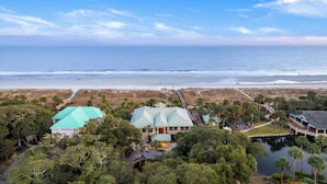 Une propriété située sur la côte, avec une grande maison dotée d’un toit végétalisé, entourée d’une végétation luxuriante et avec une plage en arrière-plan.