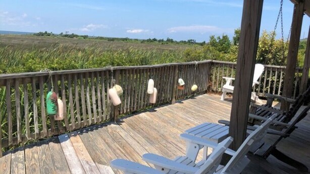 A wooden deck with white Adirondack chairs and a wooden railing overlooking a grassy field. - Soundfront Sunsets with Private Dock, Kayaks, Large Pool, Hot Tub, Guesthouse (Salvo)
