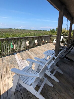 A wooden deck with white Adirondack chairs and a wooden railing overlooking a grassy field. - Soundfront Sunsets with Private Dock, Kayaks, Large Pool, Hot Tub, Guesthouse (Salvo)