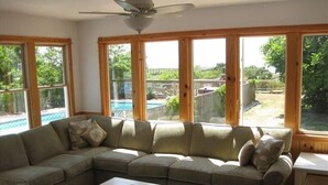 A living room with a sectional sofa, a coffee table, and large windows with a view of a backyard and pool. - Soundfront Sunsets with Private Dock, Kayaks, Large Pool, Hot Tub, Guesthouse (Salvo)