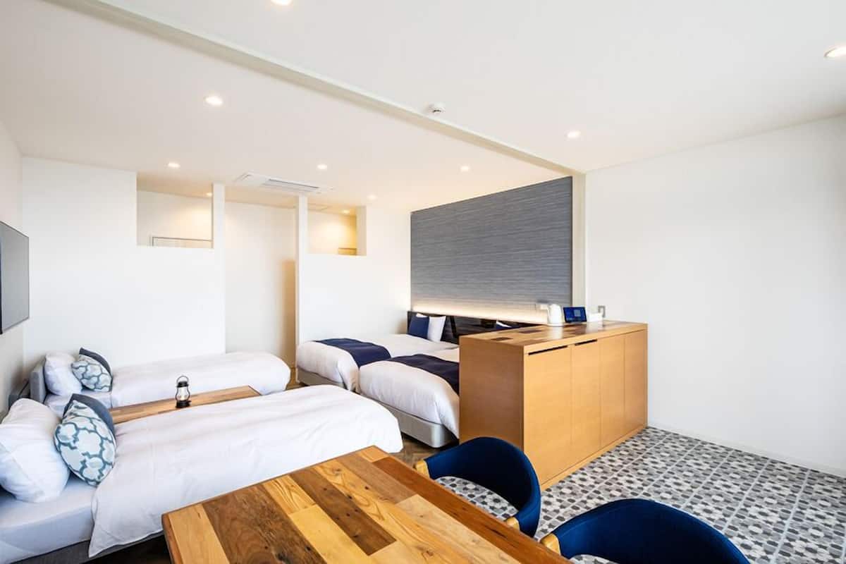 A hotel room with two beds, a wooden desk, a chair, and a small table.