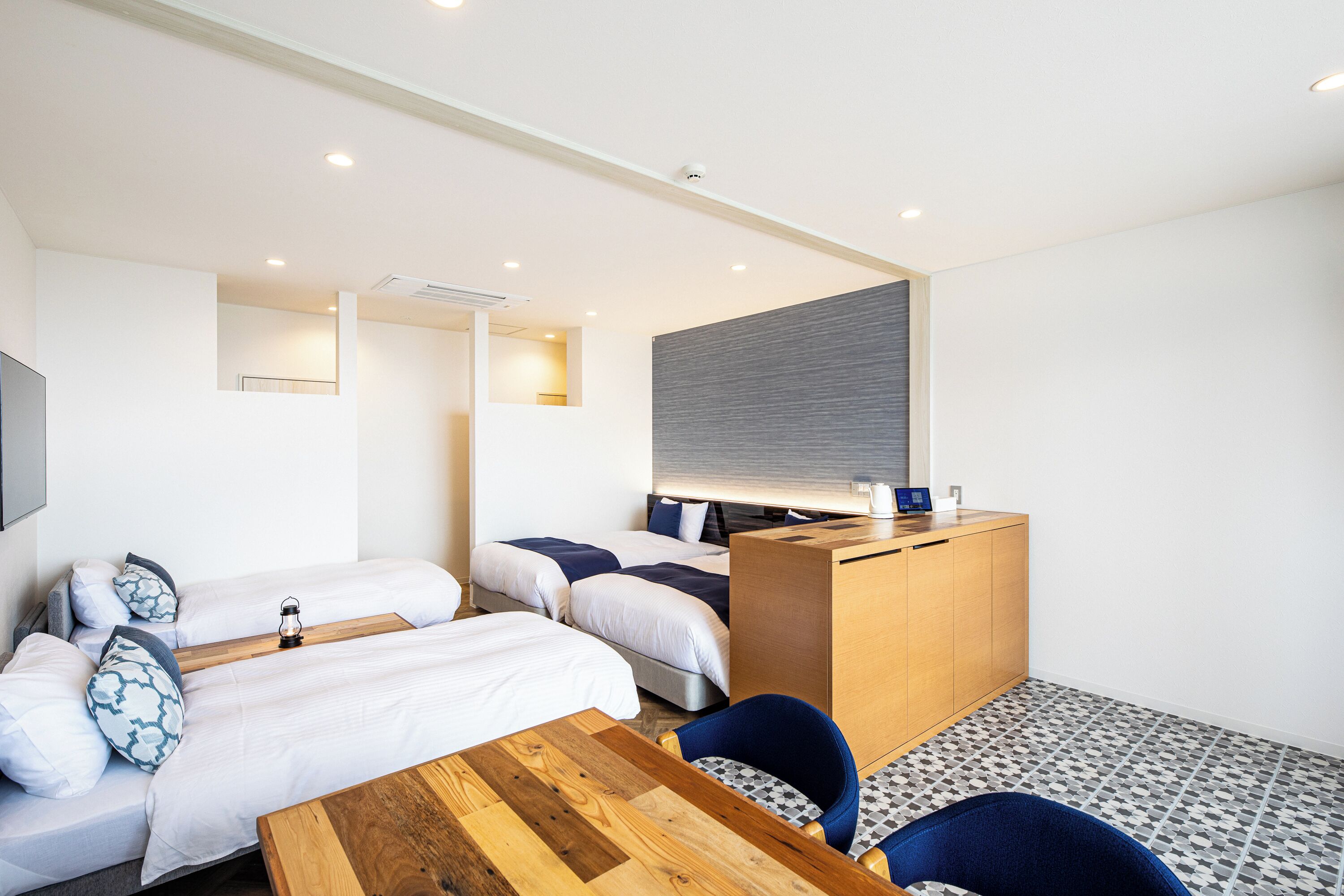 A hotel room with three beds, a wooden desk, a chair, and a small table.