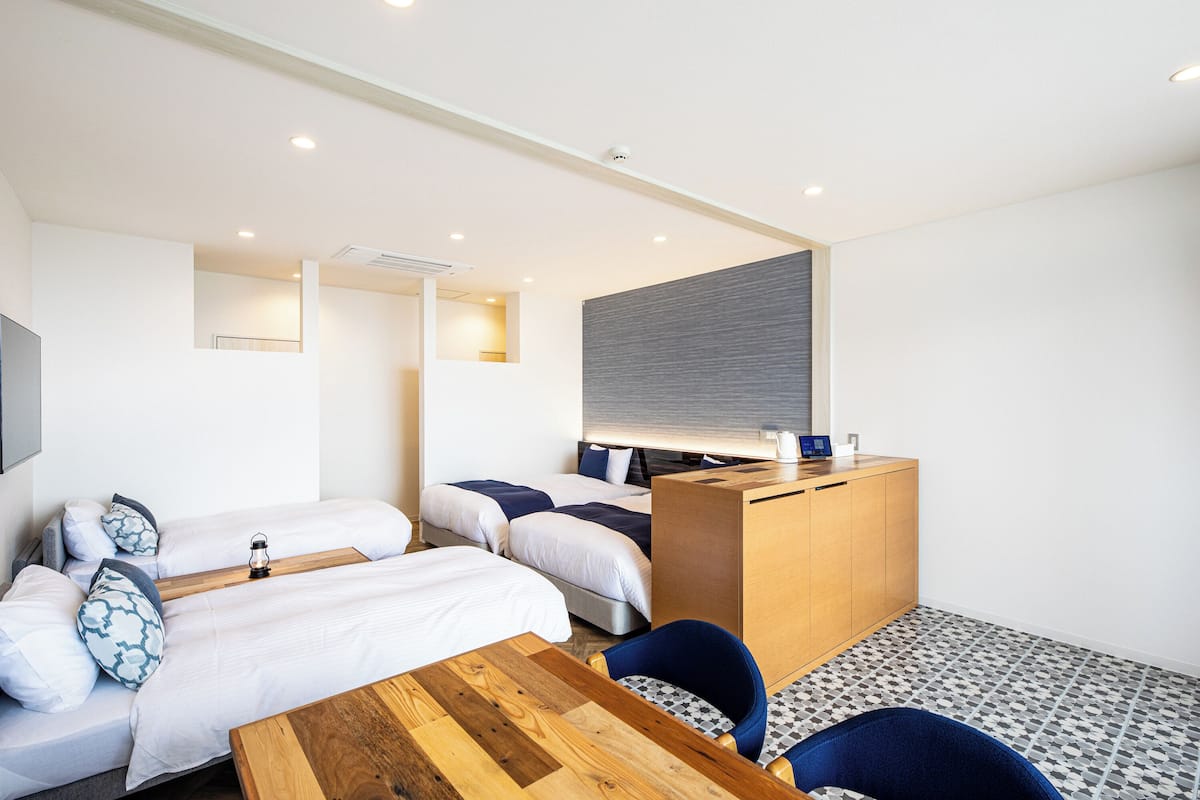 A hotel room with three beds, a wooden desk, a chair, and a small table.
