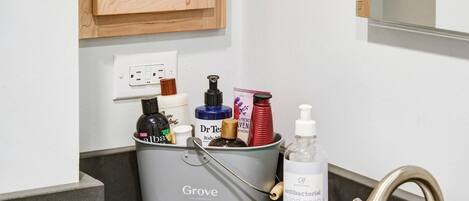 A bathroom with a grey basin containing toiletries, a bottle of antibacterial hand soap, and a mirror above the sink.
