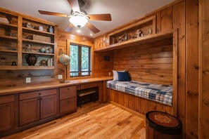 A wooden interior with a built-in bench, shelves with decorative items, and a ceiling fan.