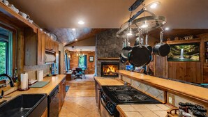 A kitchen with a central island, a stove, hanging pots, and a stone fireplace. - Heartland Lodge: Multi-fam cabin in Hocking Hills (Logan)