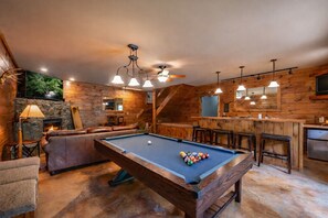 A cozy indoor setting with a pool table, leather seating, a bar area, and a fireplace.