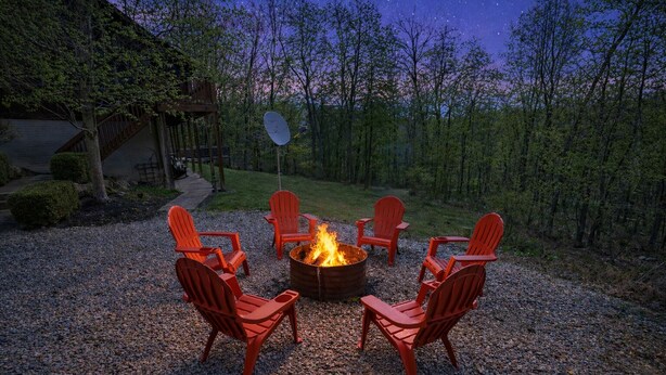 A fire pit with red chairs arranged around it, set on a gravel surface with trees in the background. - Heartland Lodge: Multi-fam cabin in Hocking Hills (Logan)
