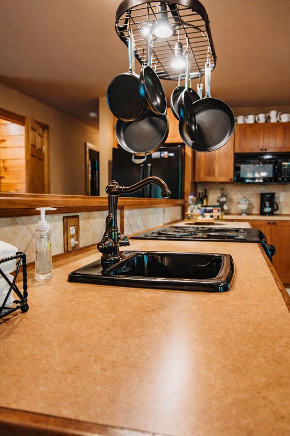 A kitchen with a modern faucet, a hanging pot rack, and a countertop with a soap dispenser.