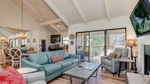 A spacious living room with a blue sofa, a coffee table, and a fireplace. There is a kitchen in the background with a microwave and a dining area. - Cozy condo in Big Canoe! - Misty Ridge (Jasper)