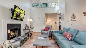 A modern living room with a fireplace, a television mounted on the wall, a blue sofa, and a coffee table. - Cozy condo in Big Canoe! - Misty Ridge (Jasper)