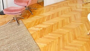 Un saló modern amb una cadira rosa, un moble blanc i una televisió penjada a la paret.