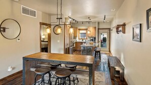 Una cocina con una isla central, taburetes de madera, iluminación colgante y vistas al área de comedor.