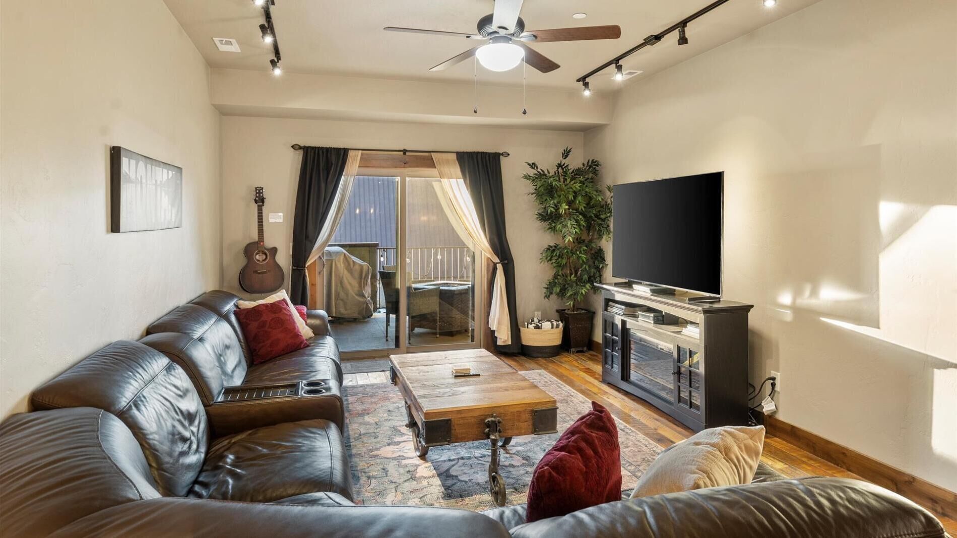 A modern living room with a leather sofa, a coffee table, a TV, and a guitar.