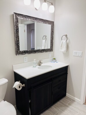 Une salle de bain avec un lavabo blanc, des meubles noirs, un miroir avec un cadre en mosaïque et un porte-serviettes.