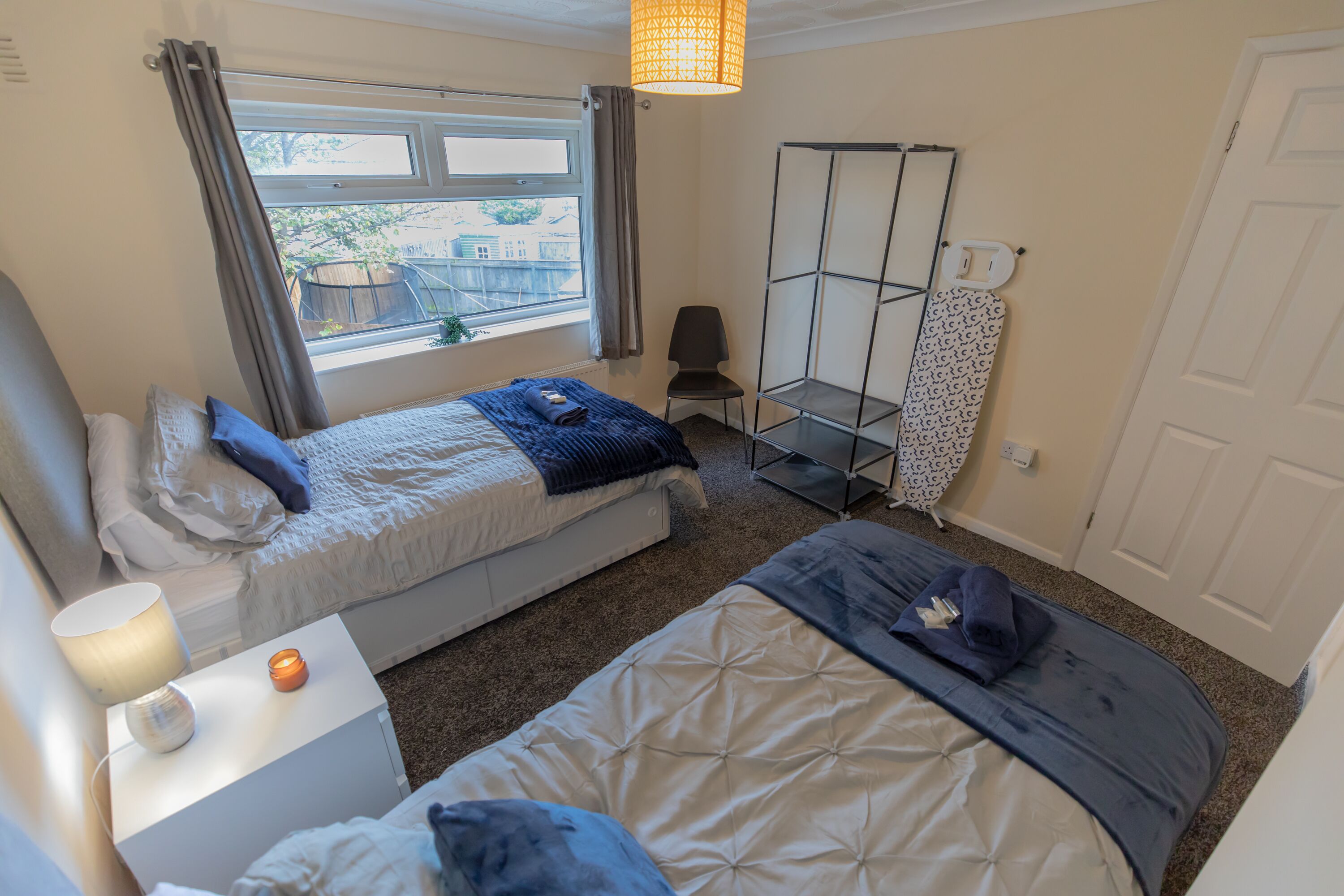 A bedroom with two beds, a chair, a shelf, and a window.