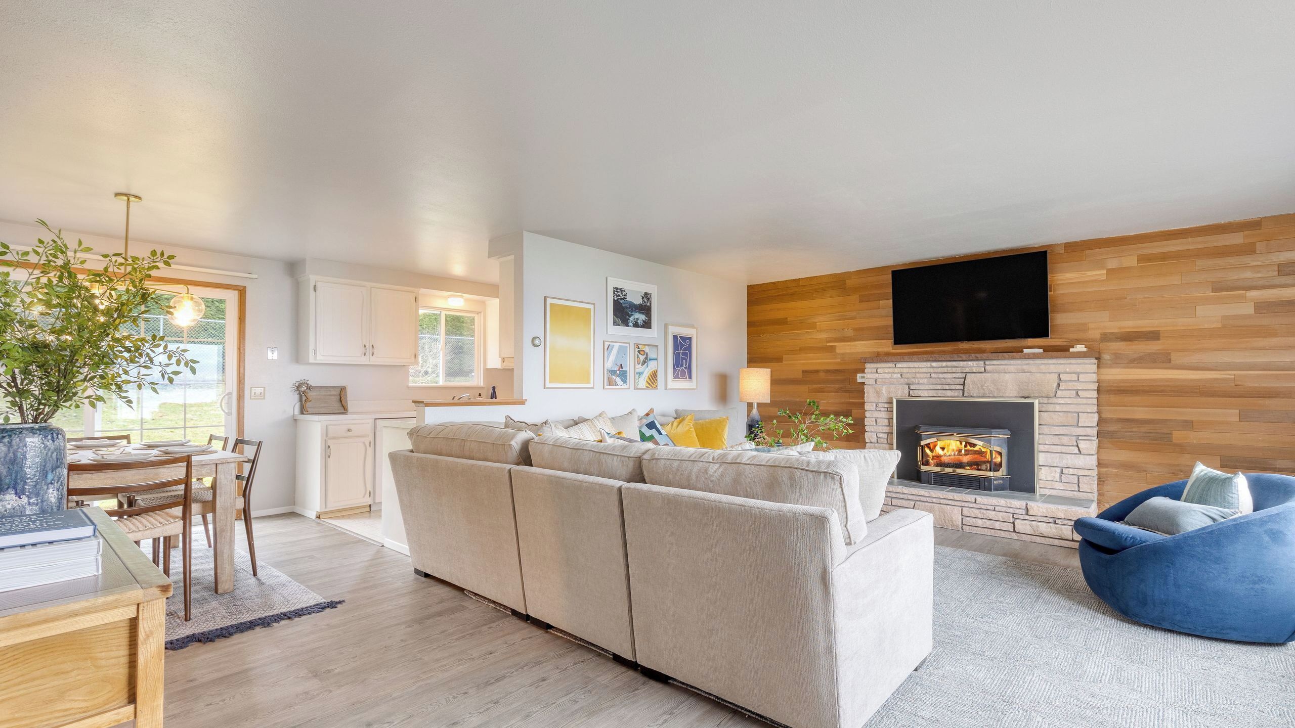Ein modernes Wohnzimmer mit einer Couch, einem Essbereich mit Tisch und Stühlen, einem Kamin und einem an der Wand befestigten Fernseher.