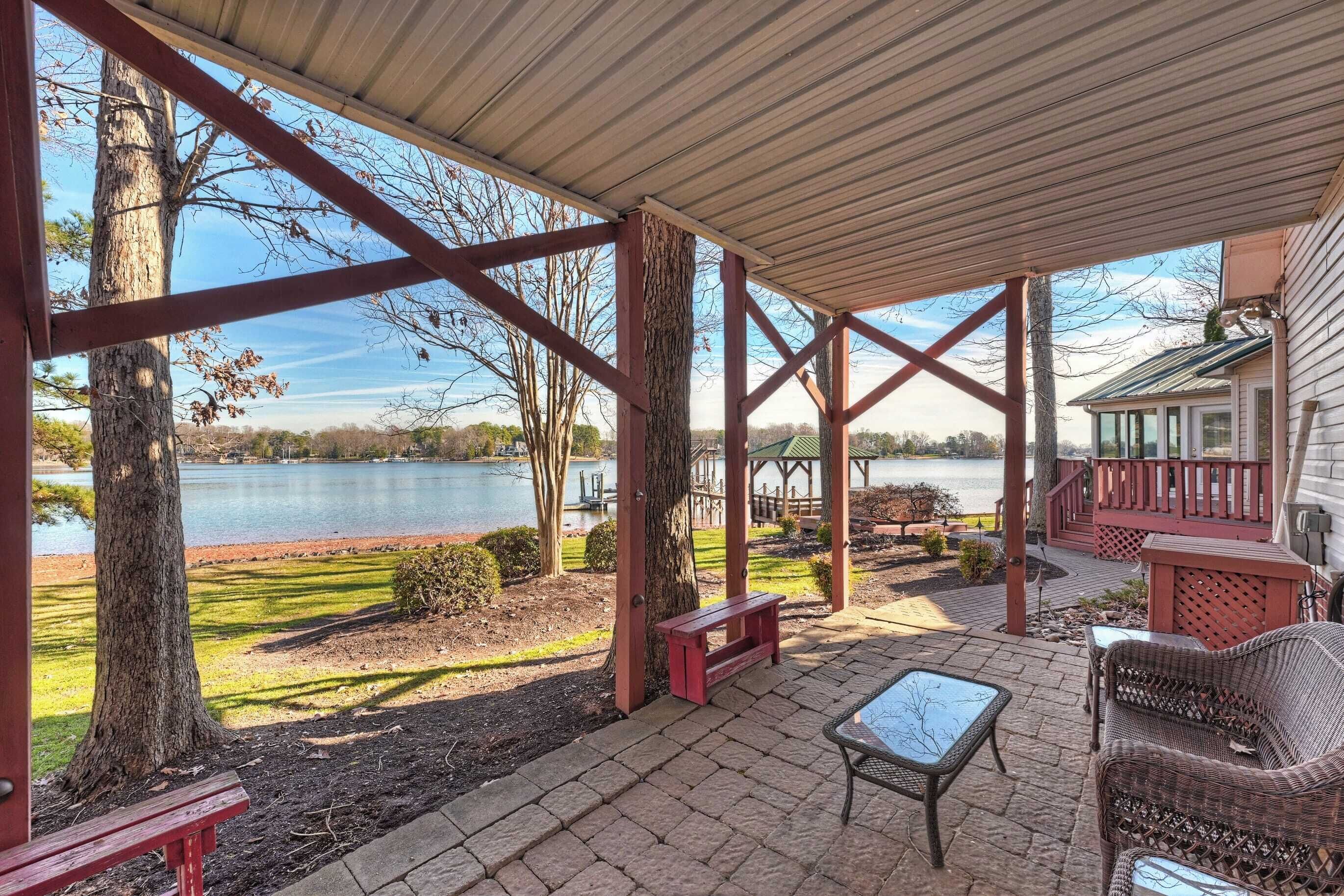 A covered patio with a view of a lake, wooden deck, and outdoor furniture.