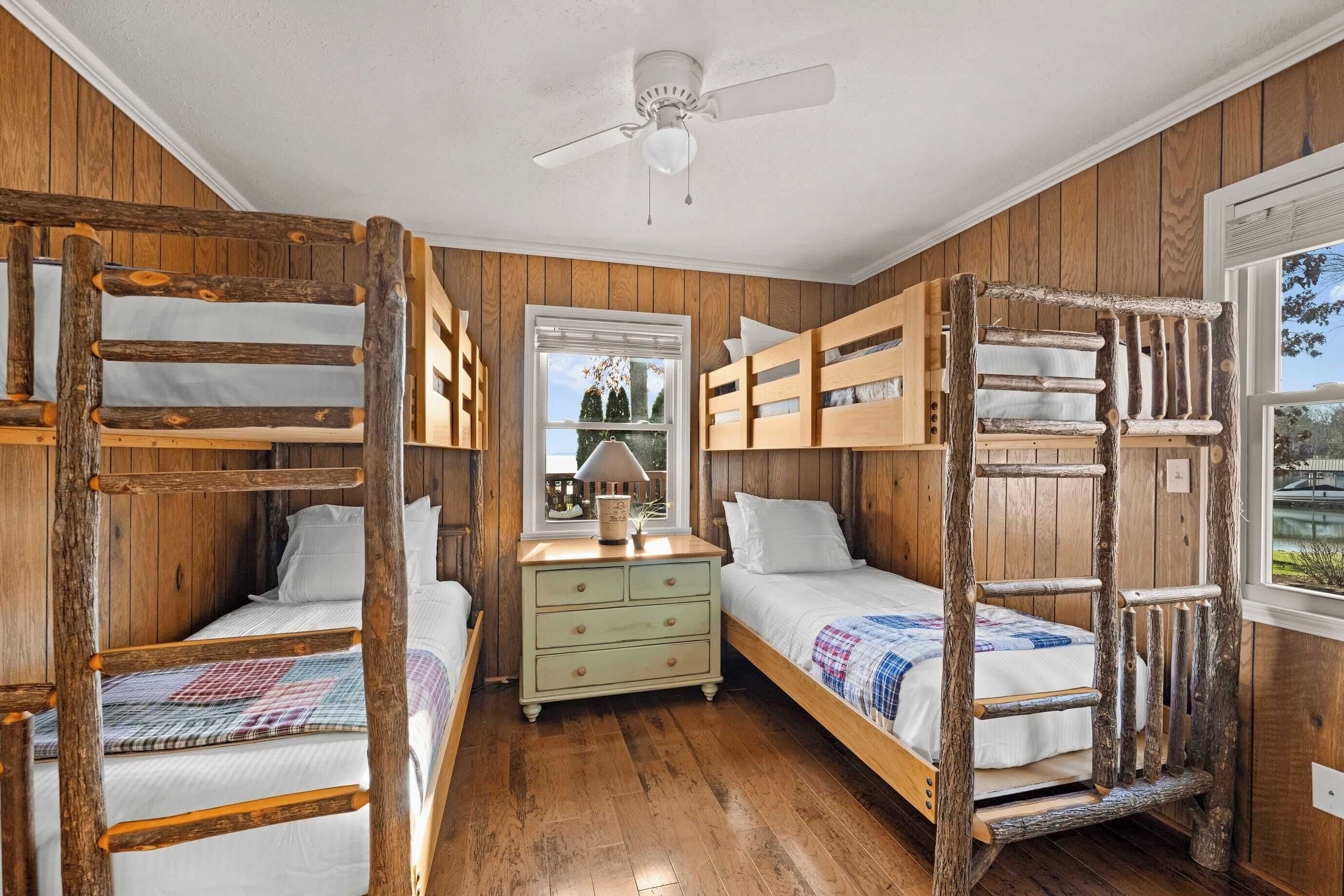 A rustic wooden room with bunk beds, a dresser, and a ceiling fan.
