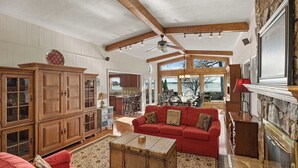 A spacious living room with a red sofa, wooden cabinets, a fireplace, and a large window offering a view of the outdoors. - Bear Creek Lodge by Avantstay Lakefront + Dock (Mooresville)