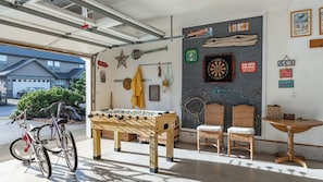A garage with a foosball table, two wicker chairs, a dartboard, and a bicycle. - Truly a Treasure by Avantstay Walk to Beach, Patio (Manzanita)