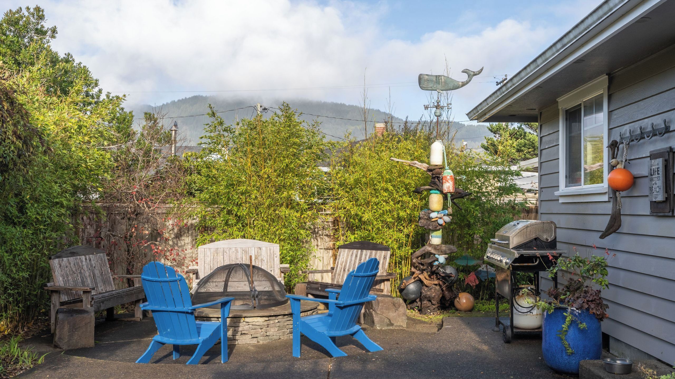 Un patio con dos sillas Adirondack azules, una parrilla de piedra y un móvil decorativo.